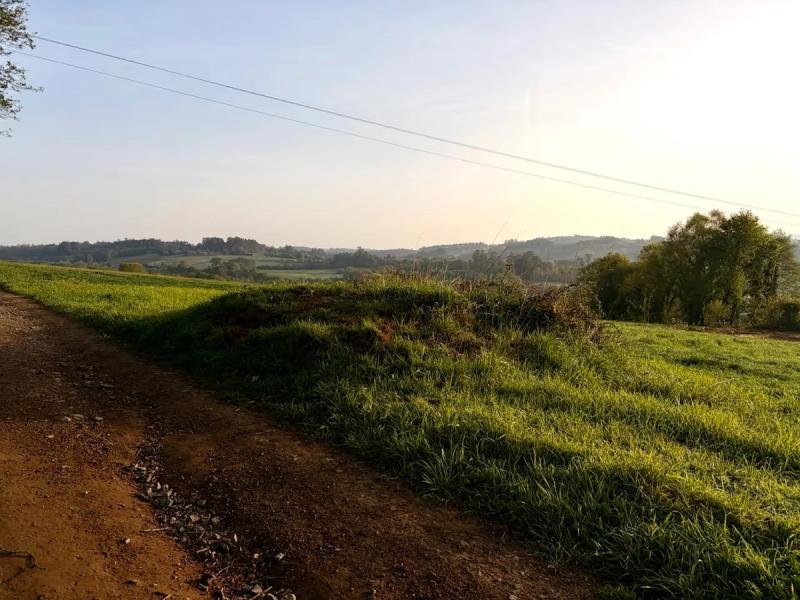 a view across open meadows in the countryside in Galicia with a brown footpath in the bottom left and open clear skies