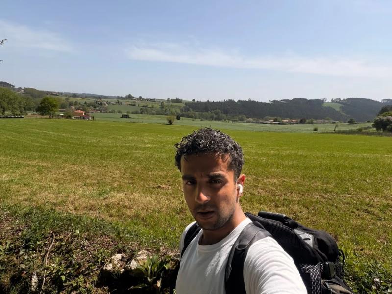 me in front of wide open meadows in the countryside. A few houses and woods are visible in the distance.