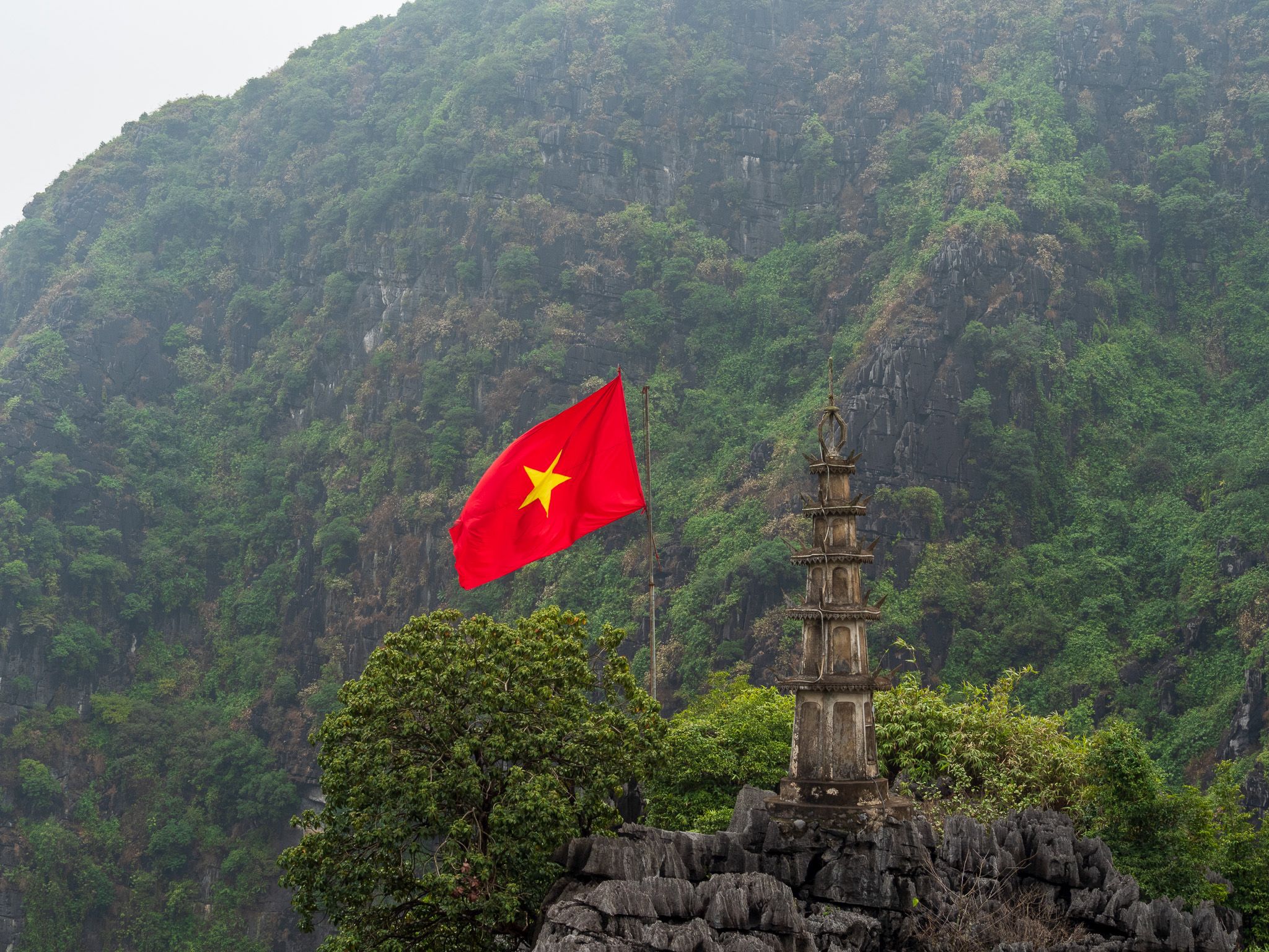 a red flag with a yellow star is flying in the wind in front of a mountain .
