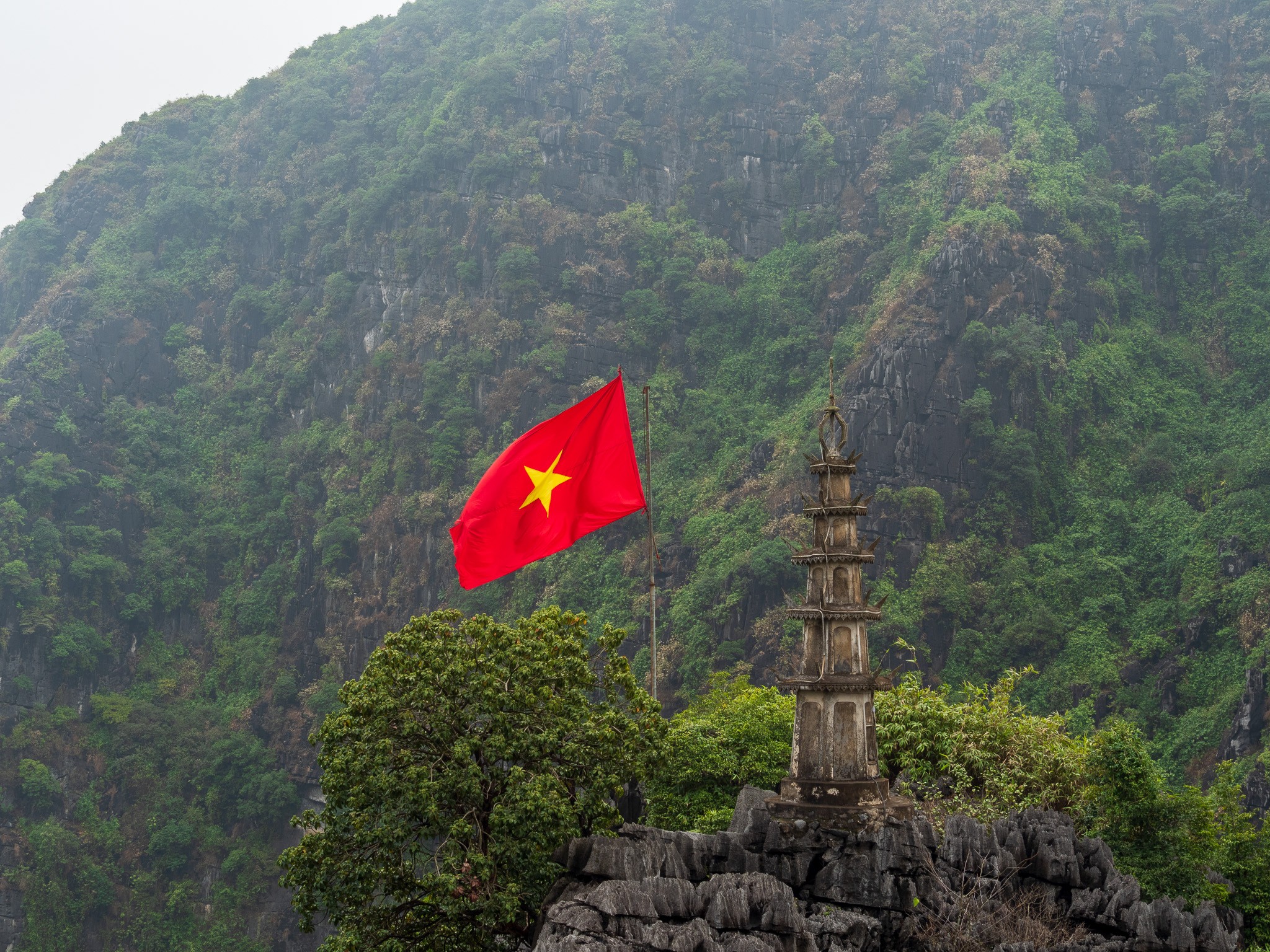 a red flag with a yellow star is flying in the wind in front of a mountain .