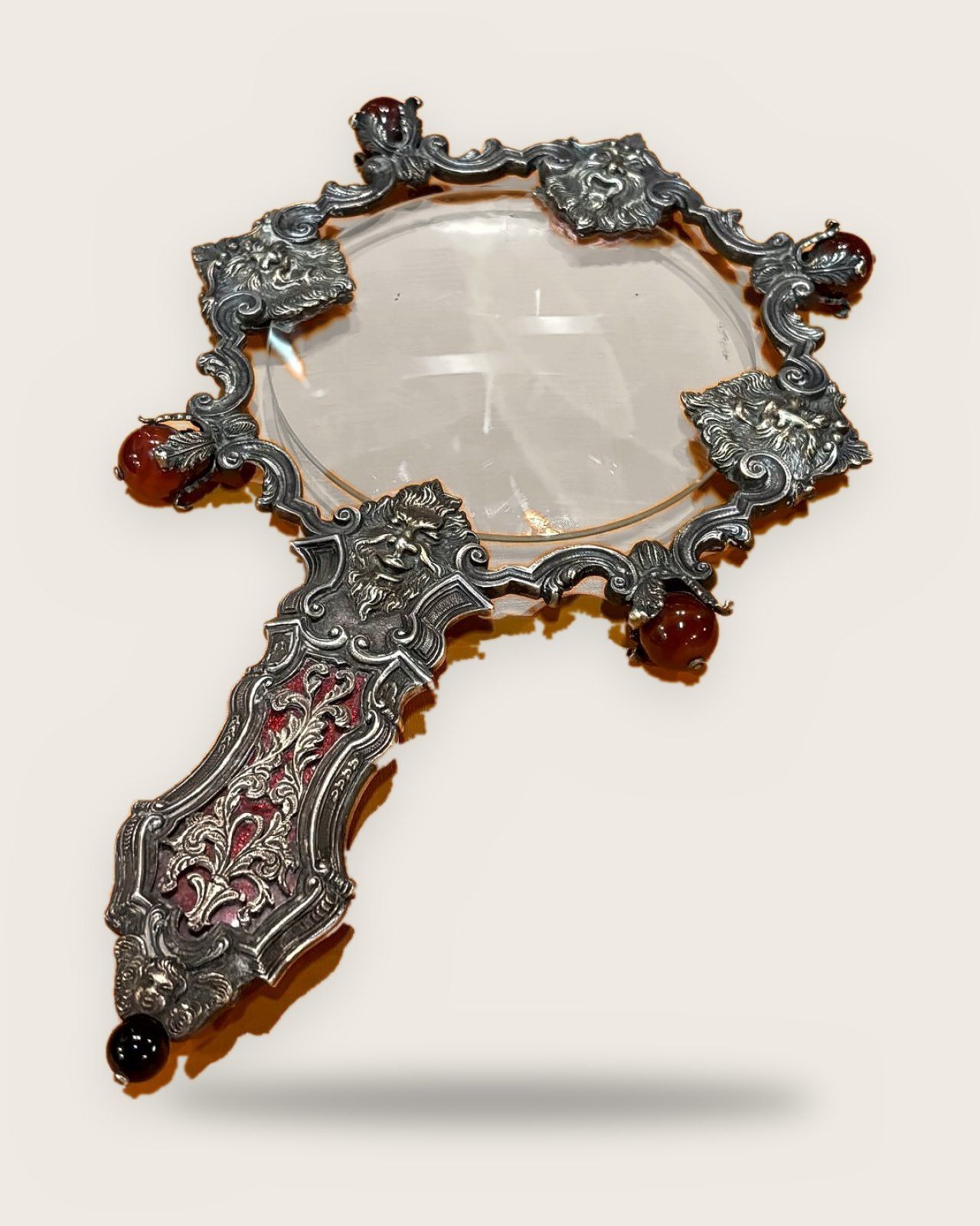 Magnifying glass with a scrolling silver frame, masks and carnelian spheres