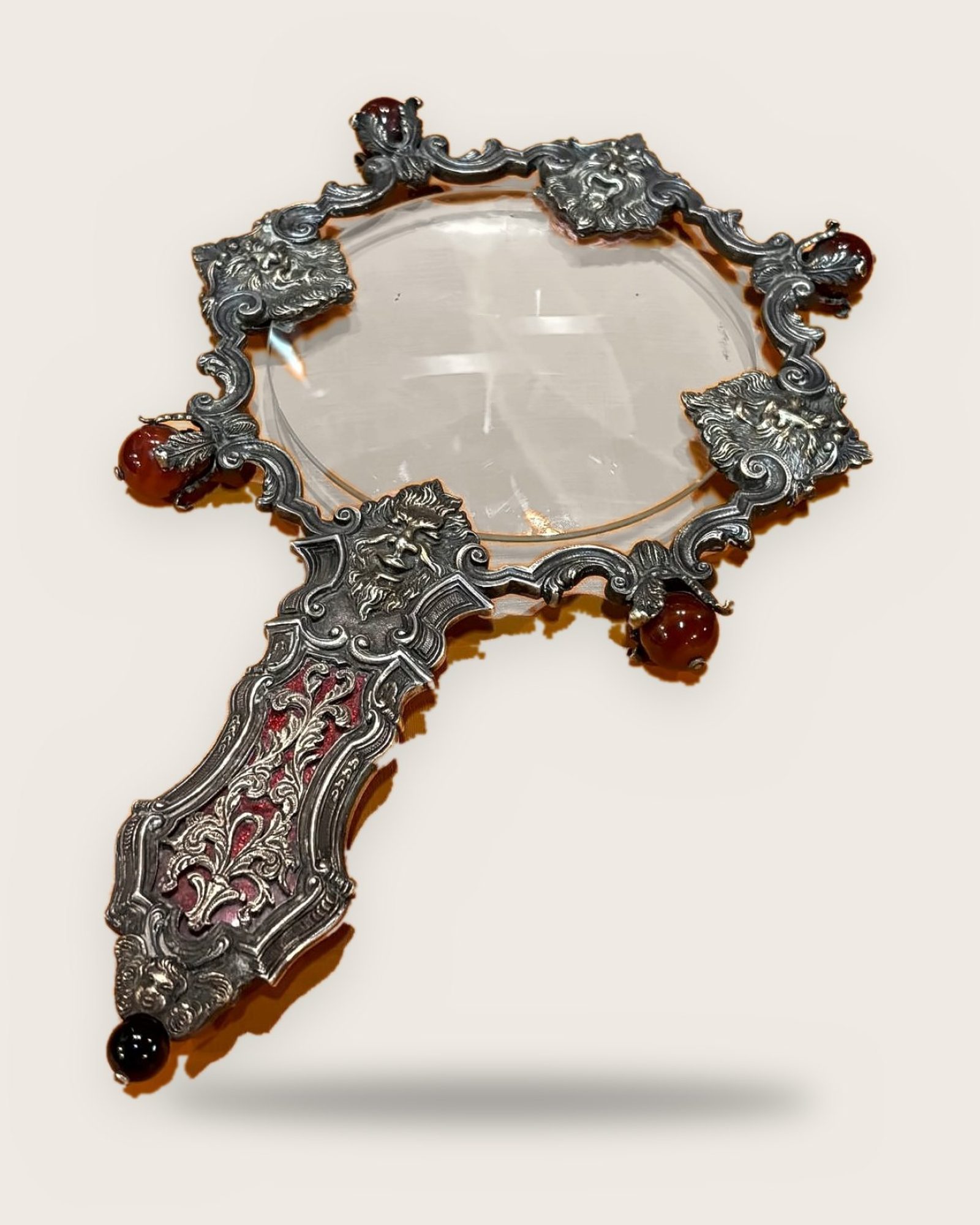 Magnifying glass with a scrolling silver frame, masks and carnelian spheres