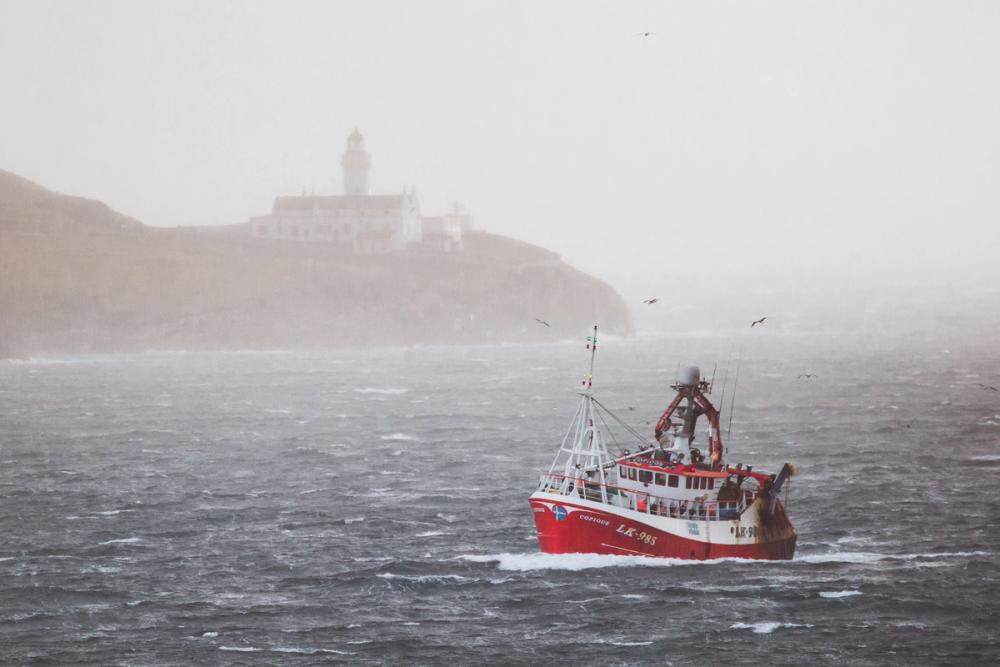 Fishing boat passing the lighthouse in a storm