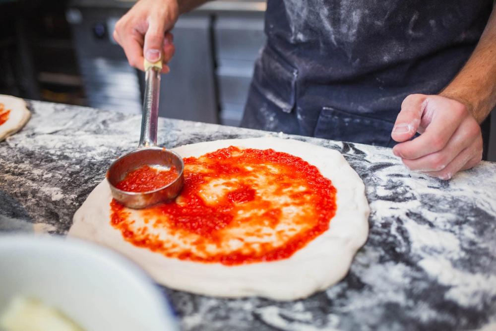 Baker adds sauce to pizza dough