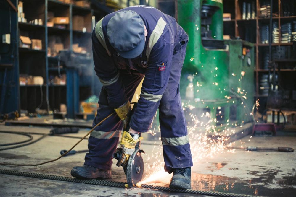 A worker cuts a wire with an angle grinder