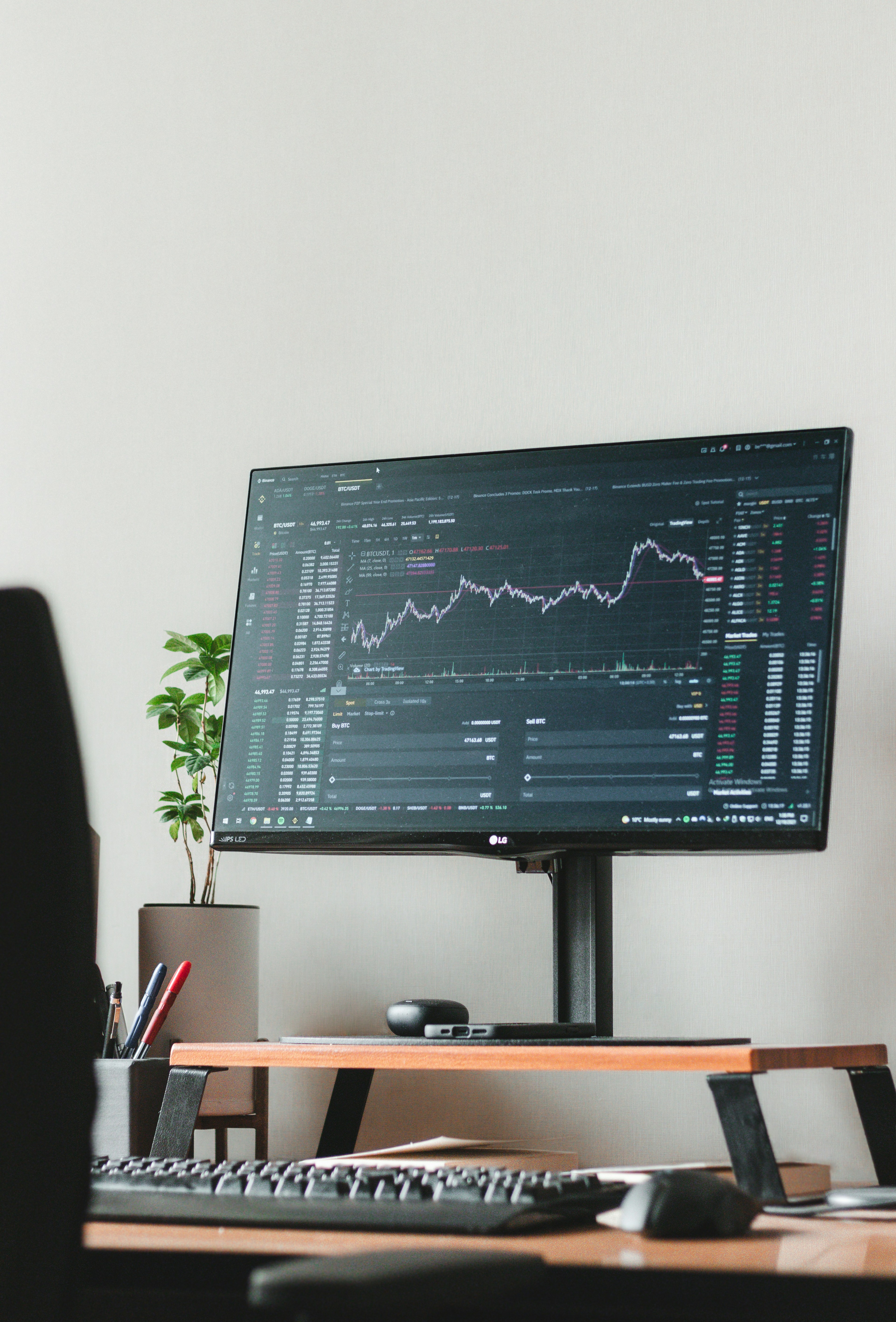 Close-up of a cryptocurrency trading screen with candlestick charts and an order book, a stylus pointing at the chart.