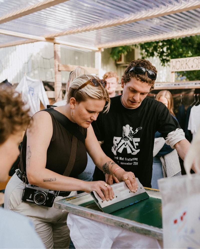 A person tries screen printing with green ink while another person supervises.