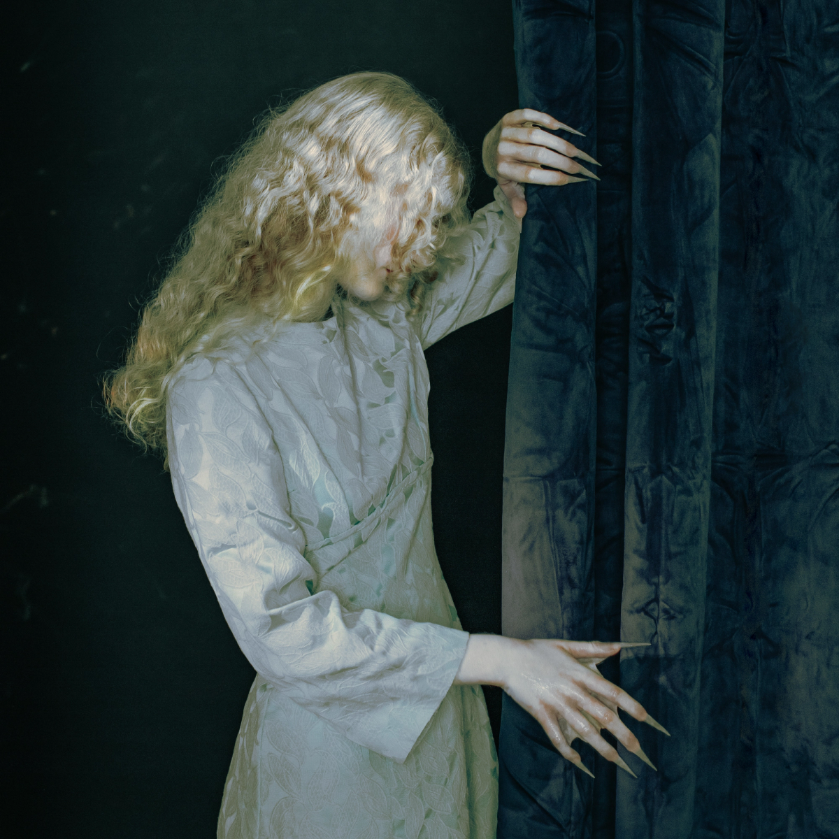 Lene 3000 looking down whilst holding a curtain with animal-like nails.