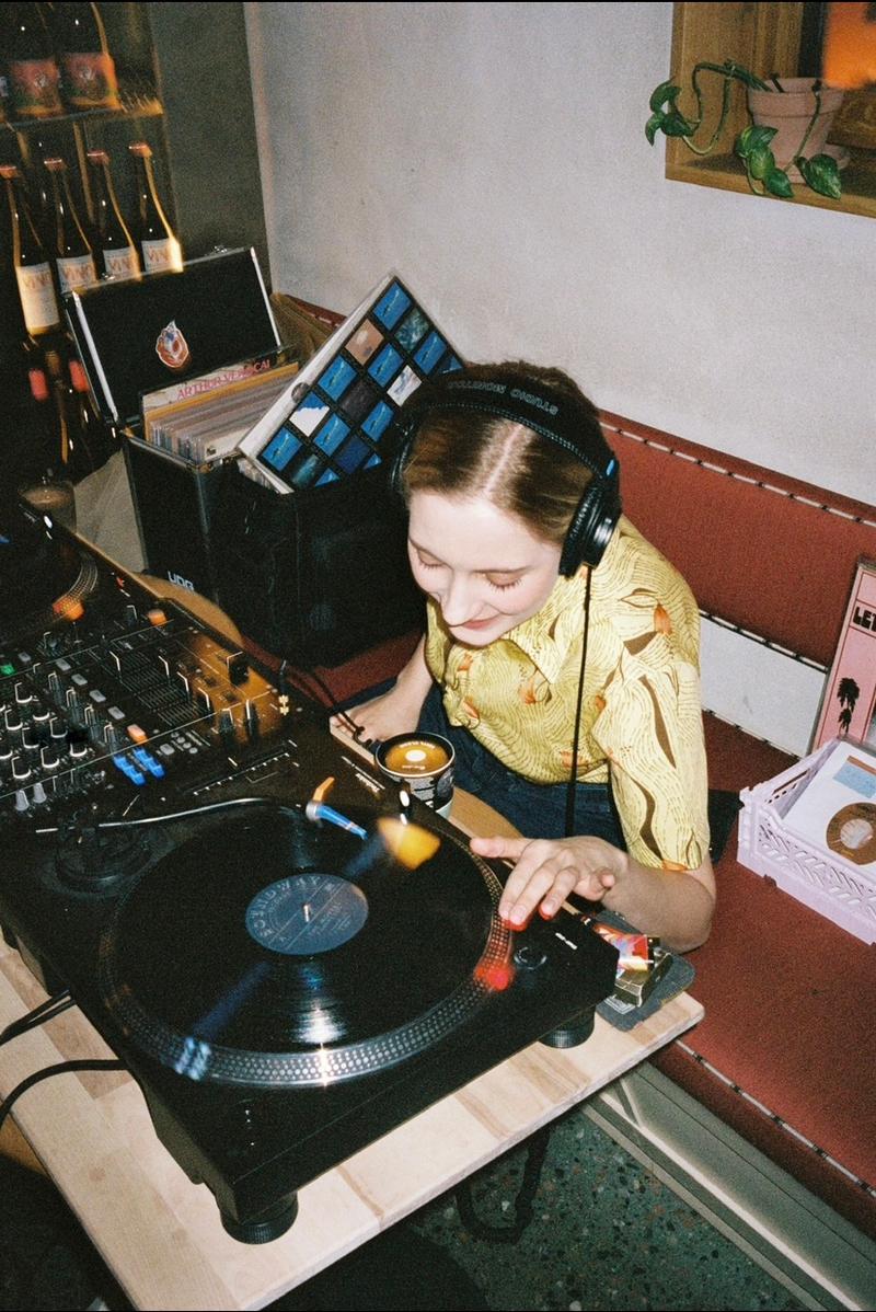 Anja Bajer smiling whilst playing a turntable next to a DJ deck.