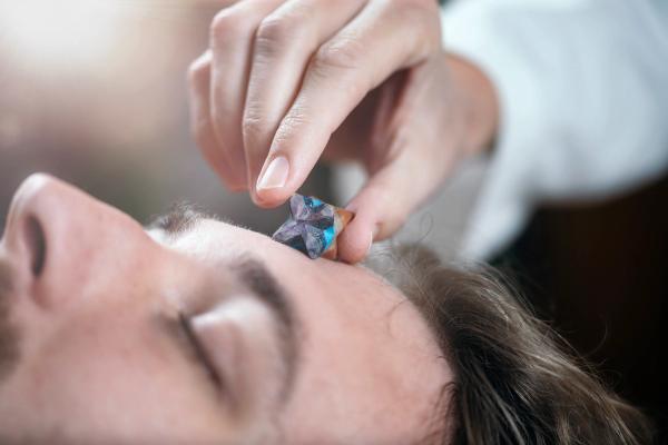 Energy healer placing a small crystal on a client's forehead during a healing session