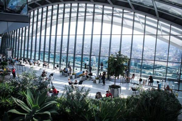 Sun-filled glass atrium garden with tropical plants and people overlooking a city skyline
