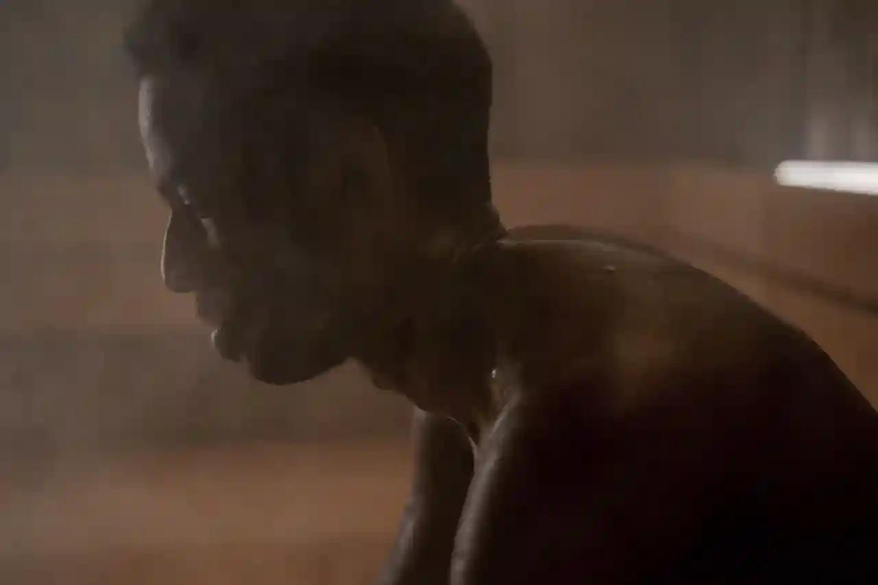 A man sits with his head lowered in a dimly lit, steam-filled wood-panelled room.