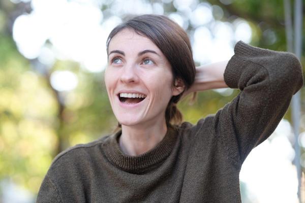 Smiling woman in a cozy sweater outdoors, looking up with a relaxed, hopeful expression
