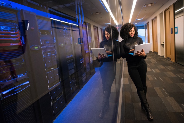 A woman leans against a wall of data servers on a laptop.