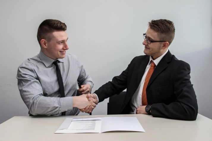 Two men in a gray office shaking hands over a contract.