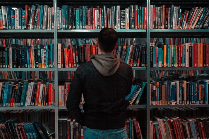 A man standing in front a bookcase at a library, perhaps the most traditional knowledge management tools