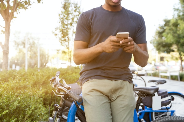 Man leaning against a bike, messaging on his phone