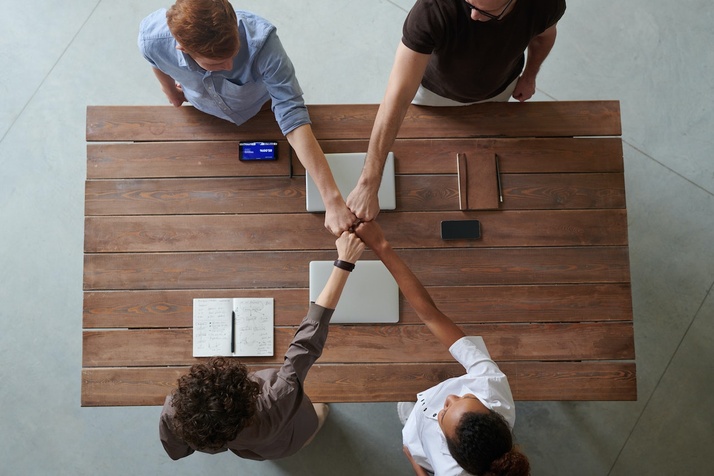 A business team fist-bumping across a table of closed computers