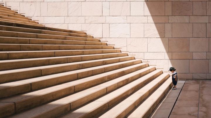 A boy stands at the bottom of a tall flight of stairs, unsure of whether to take the challenge