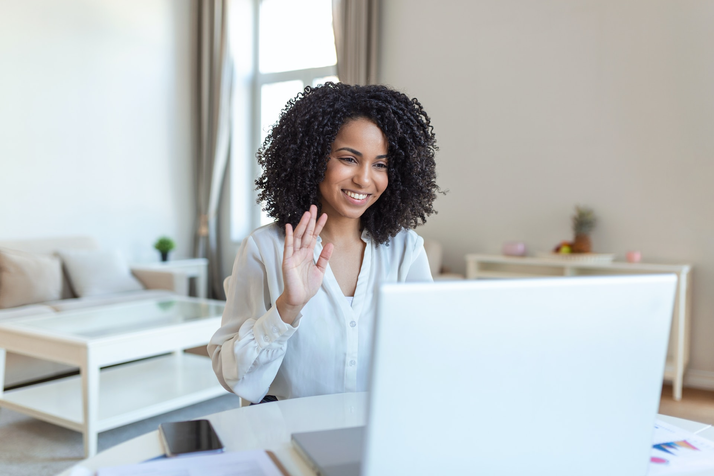 A lady smiles and waves at her laptop during a video onboarding call