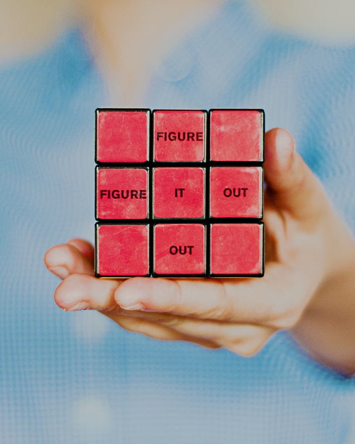 A hand holding a red rubik's cube with inspirational quote 'figure it out' spelt out