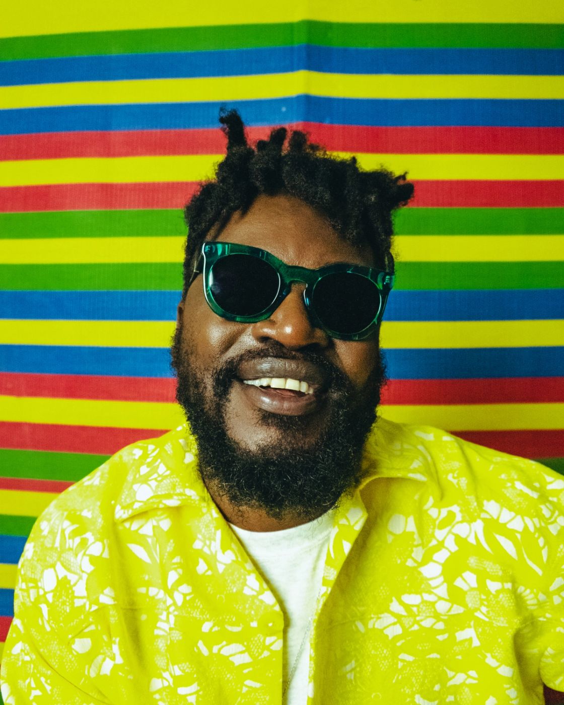 A portrait of musician Blinky Bill wearing sunglasses taken against a colourful striped background