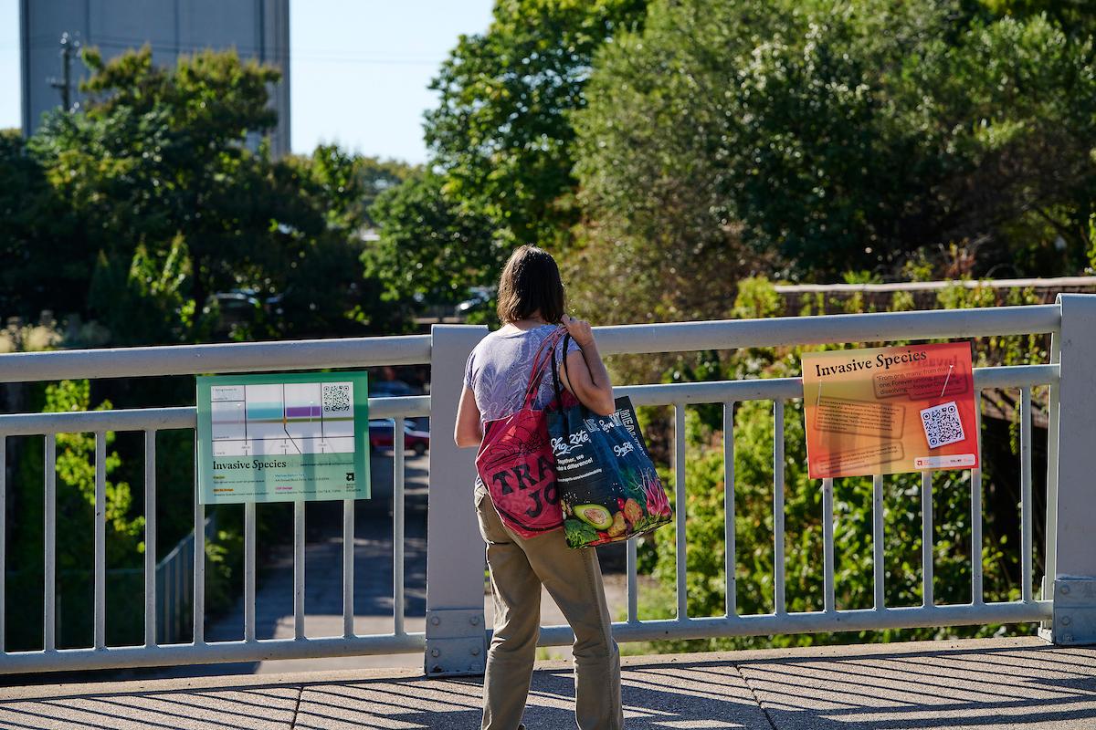 Photo courtesy of Albert Yee. Women holding bags looking out over bridge with Invasive Species signs.