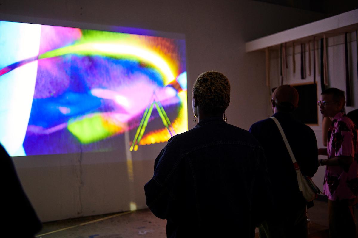 Photo by Albert Yee. Multiple people stand in a dimly lit gallery looking at an abstract video art installation.