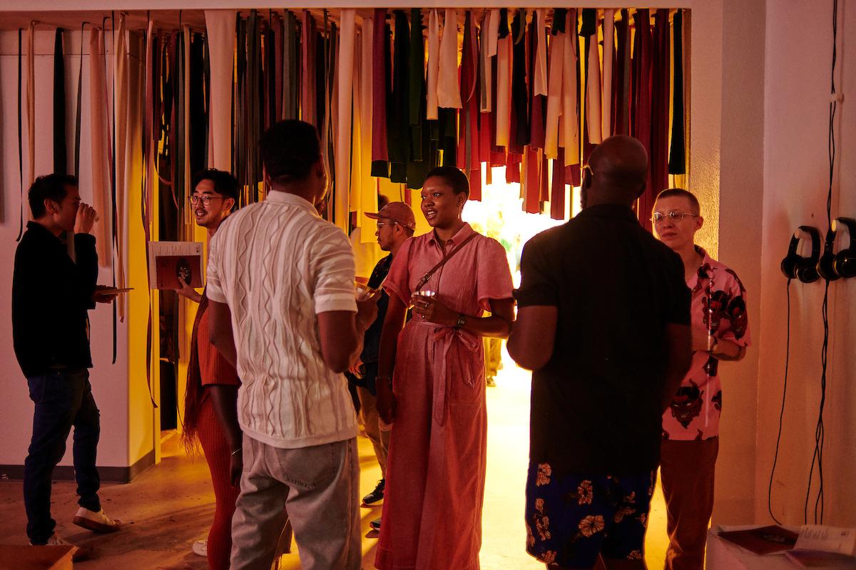 Photo courtesy of Albert Yee. Group of people at the Invasive Species opening chat in front of hanging strips of fabric.