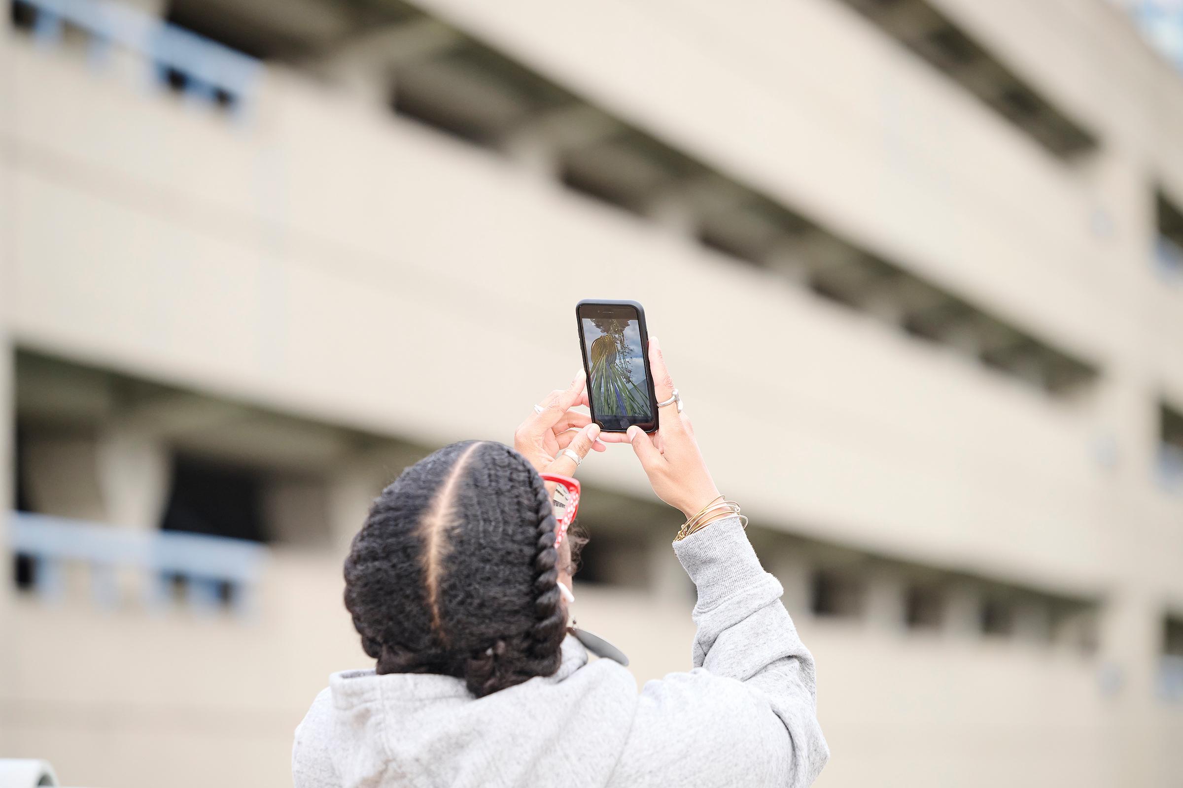 Photo courtesy of Albert Yee. Person holding up phone outside to see the digital Invasive Species exhibit.