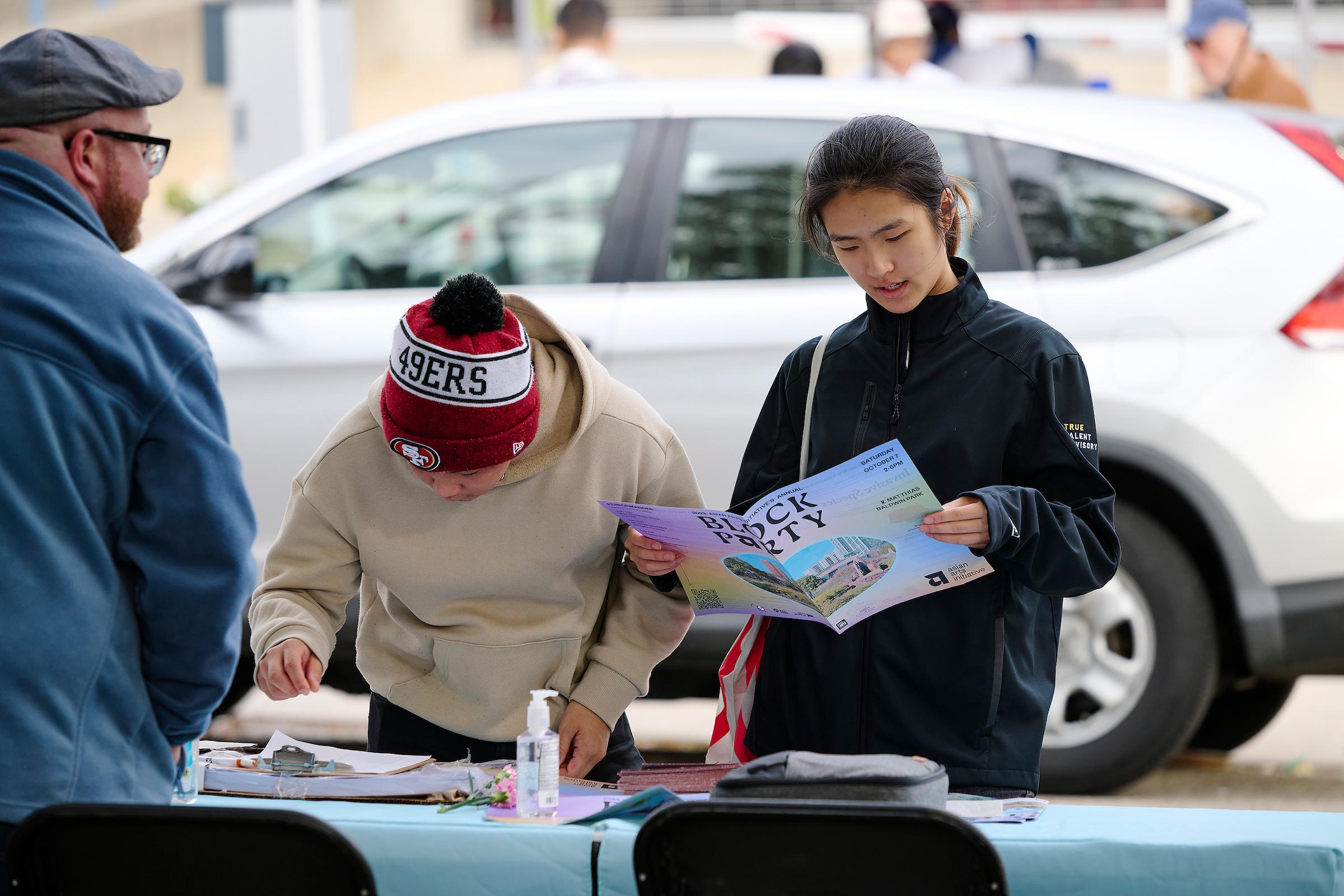 Photo courtesy of Albert Yee. People at the AAI Block party information booth looking at pamphlet.