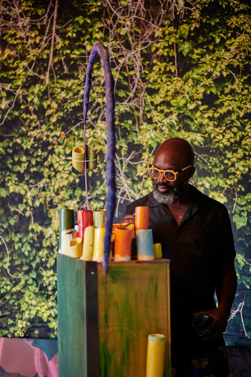 Photo by Albert Yee. A man looks over a sculptural art installation with a background of natural overgrowth on the wallpaper.