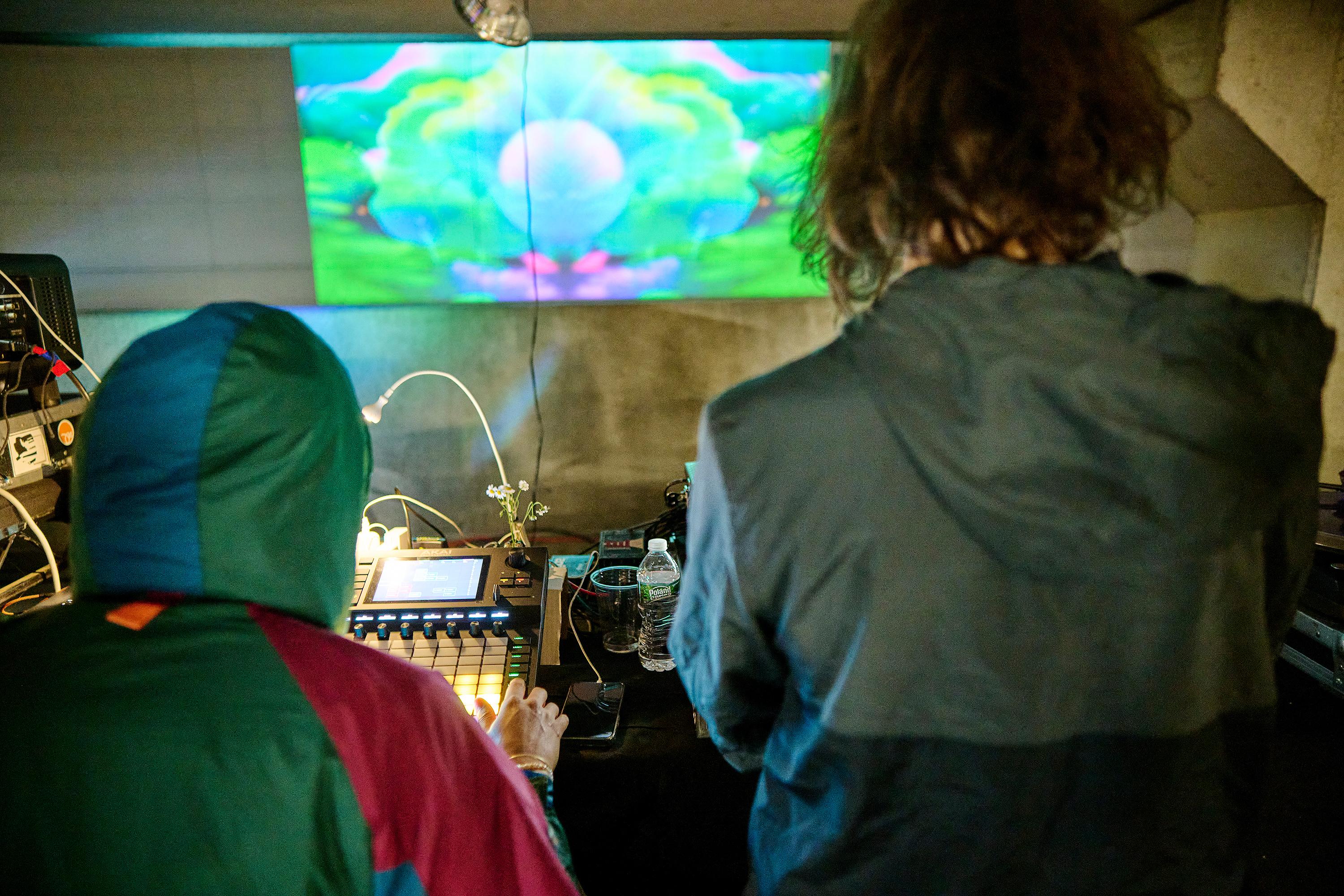 Photo courtesy of Albert Yee. 2 people with equipment in front of them with the exhibit projection in front of them outside.