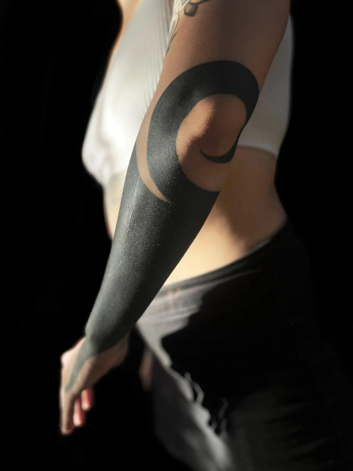 Sleek blackout arm tattoo with a bold curved negative-space design, executed in Arturo's precise blackwork style at OEK Factory Berlin.