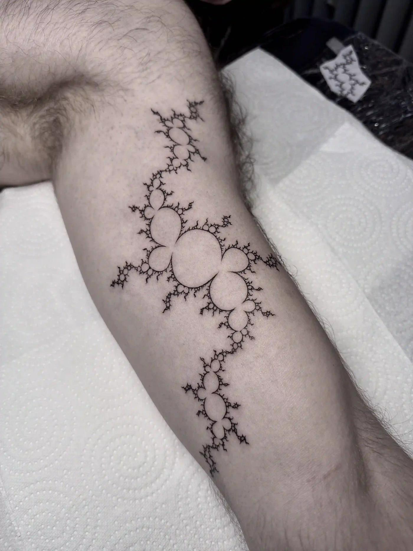 Fineline-Fraktal-Tattoo aus verzweigten kreisförmigen Formen und geometrischer Symmetrie, präzises schwarzes Linework am Bein.