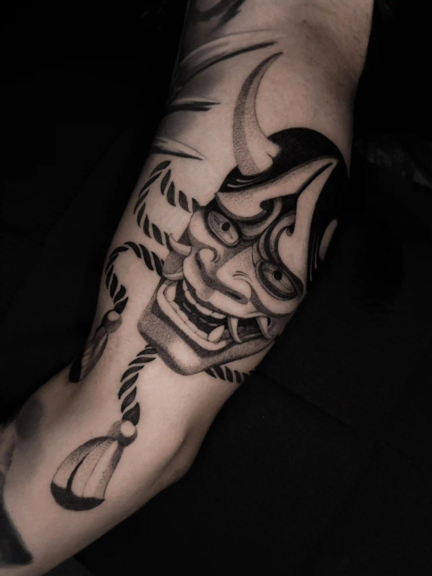 Tattoo einer japanischen Hannya-Maske mit kräftiger schwarzer Schattierung und Seil-Details, mit intensivem Ausdruck und traditioneller Dotwork-Textur am Oberarm.