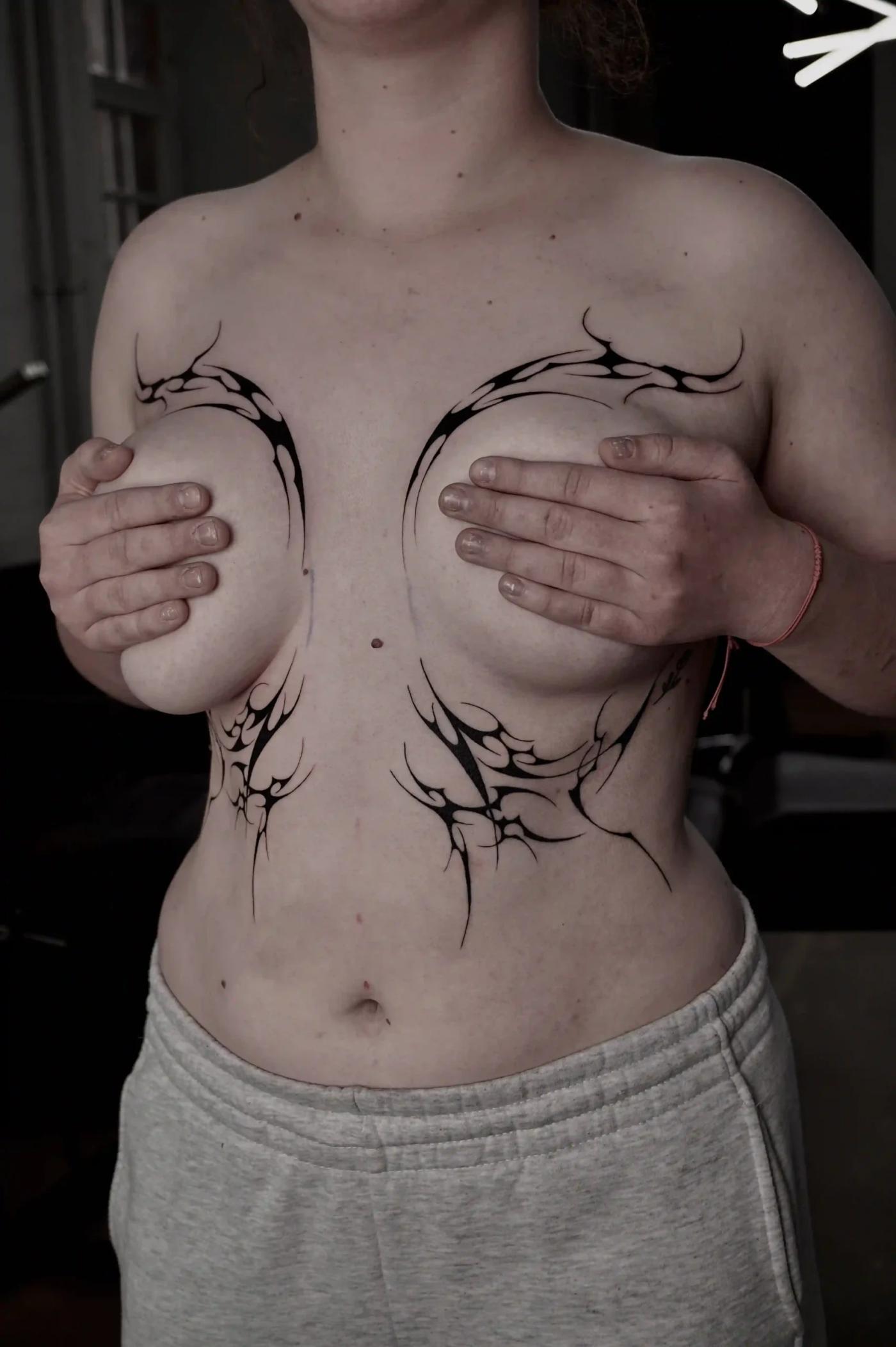 Abstraktes Cyber-Sigilism-Tattoo um die Brust und darunter, aus gespiegelten, flammenartigen Formen mit kräftigem Kontrast und klarem Negativraum.