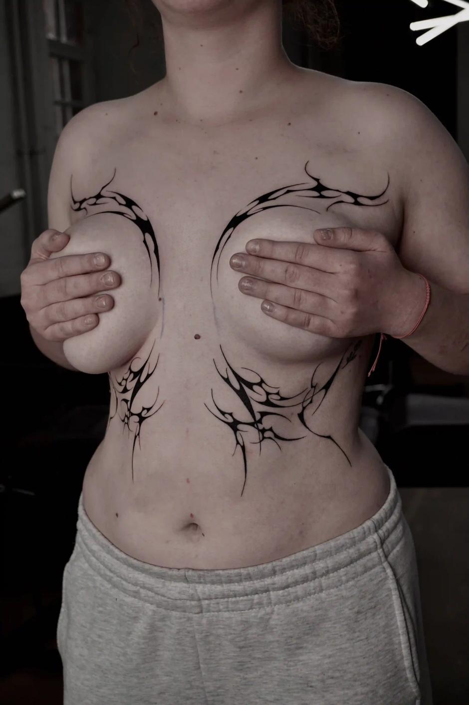 Abstraktes Cyber-Sigilism-Tattoo um die Brust und darunter, aus gespiegelten, flammenartigen Formen mit kräftigem Kontrast und klarem Negativraum.