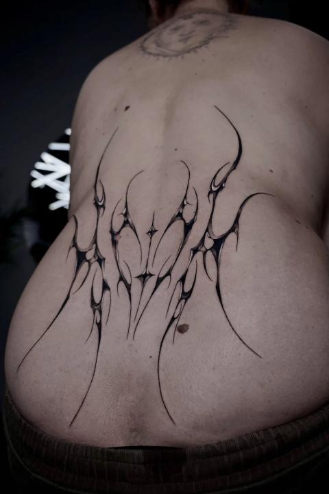 Abstraktes Cyber-Sigilism-Tattoo am unteren Rücken aus scharfen, symmetrischen flammenartigen Formen mit sanften Verläufen und Negativraum-Akzenten.