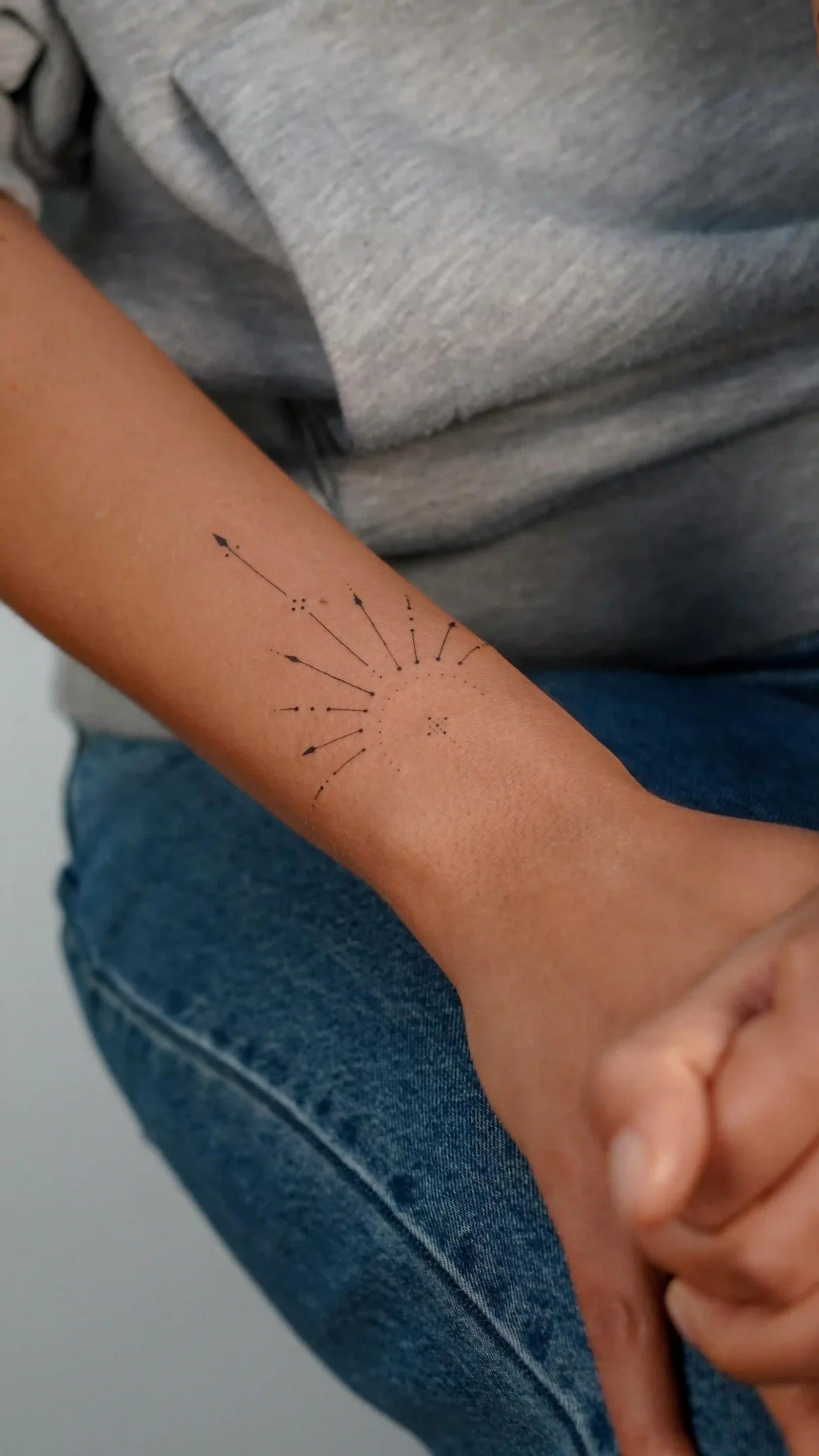 Minimalistisches Fineline-Tattoo einer Sonne mit Strahlen am Unterarm