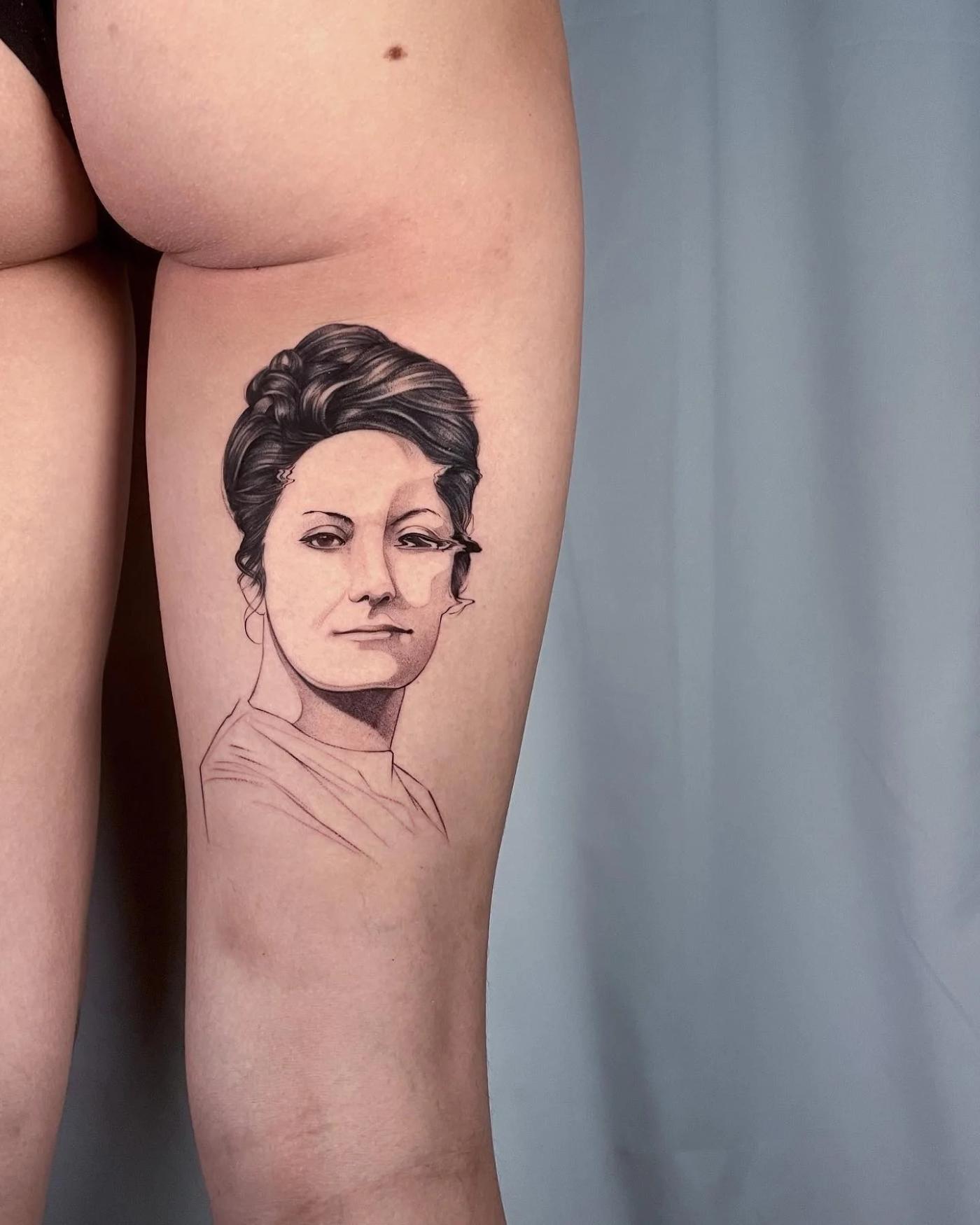 Schwarz-Grau-Porträt-Tattoo einer Frau mit weich schattierten Gesichtszügen und Fineline-Konturen am oberen Oberschenkel.