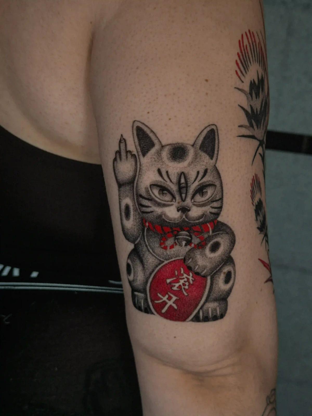 Schwarz-Grau-Dotwork-Tattoo einer Winkekatze mit roten Akzenten, das traditionelle Maneki-neko-Symbolik mit Humor verbindet, gestochen in der OEK Factory Berlin.