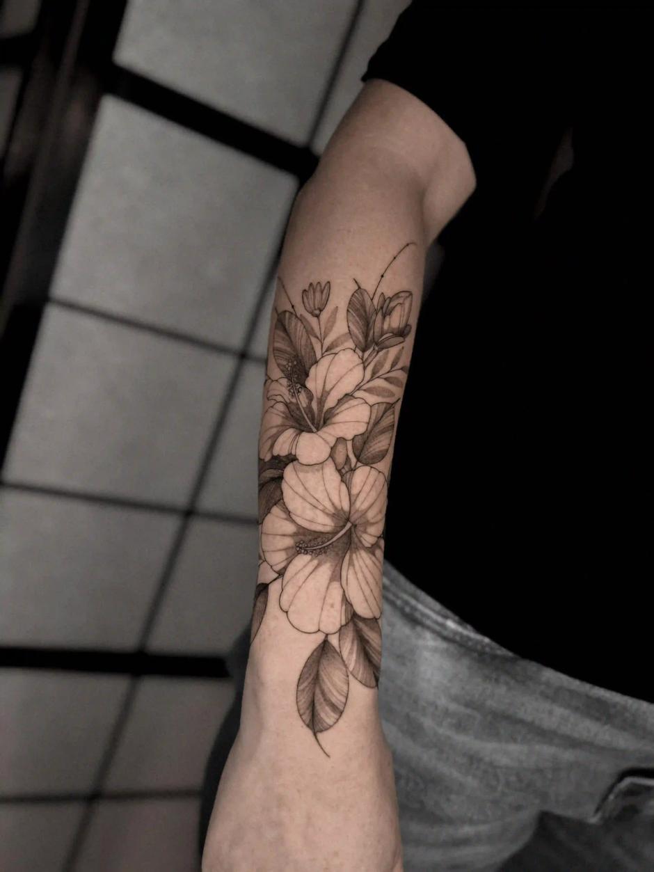 Feines Schwarz-Grau-Blumen-Tattoo am Unterarm mit geschichteten Hibiskus- und Blattkompositionen, mit subtiler Schattierung und Fineline-Realismus.