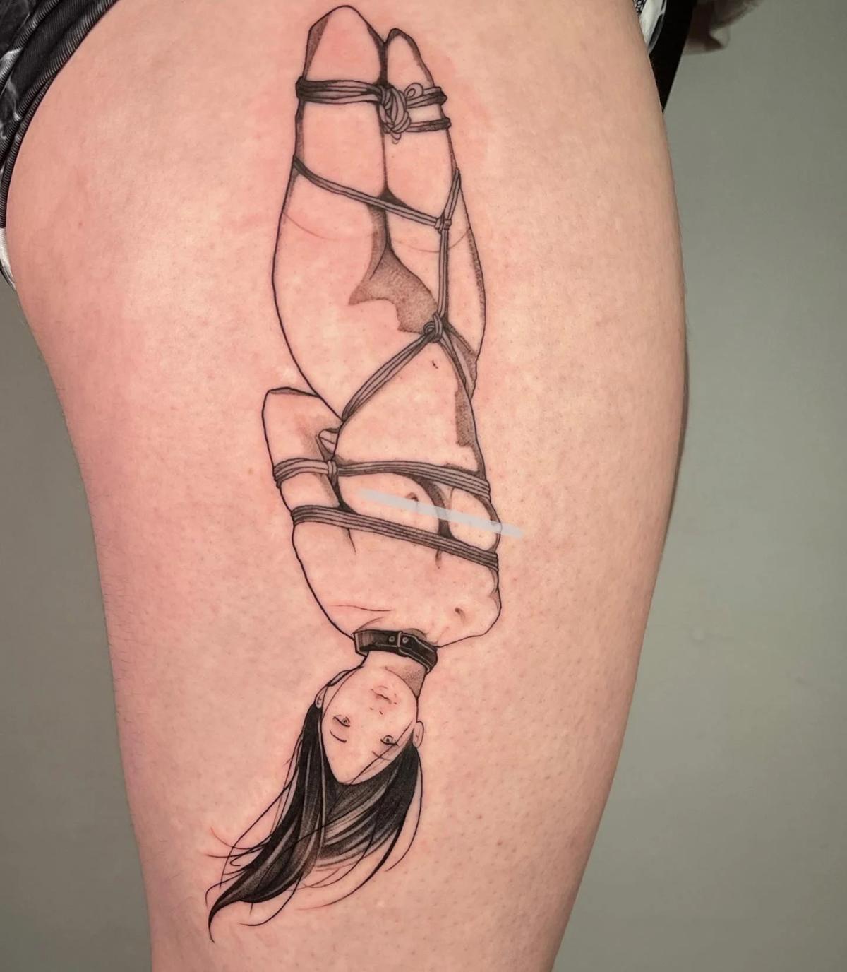 Fine-line tattoo of a bound woman in shibari rope suspension, rendered with minimal shading and delicate contours on the thigh.