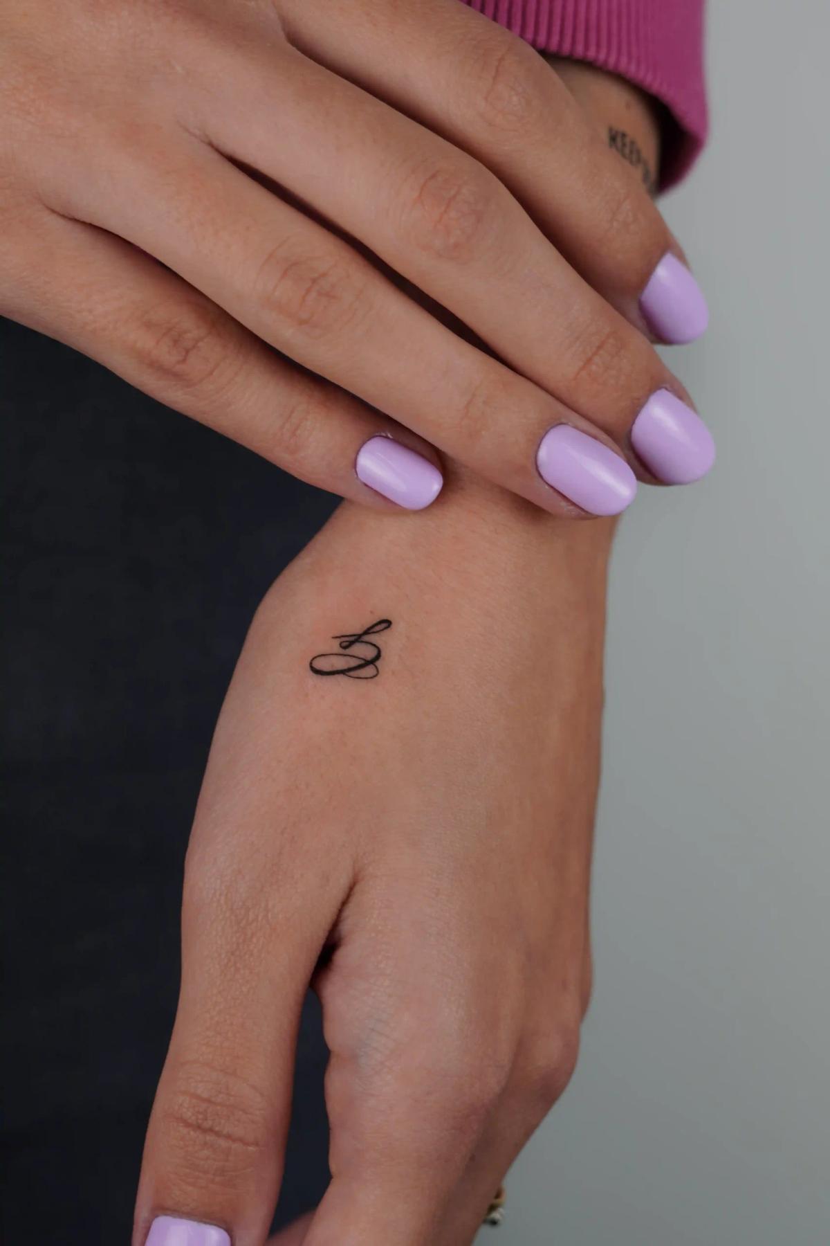 Fineline-Buchstaben-Tattoo an der Hand