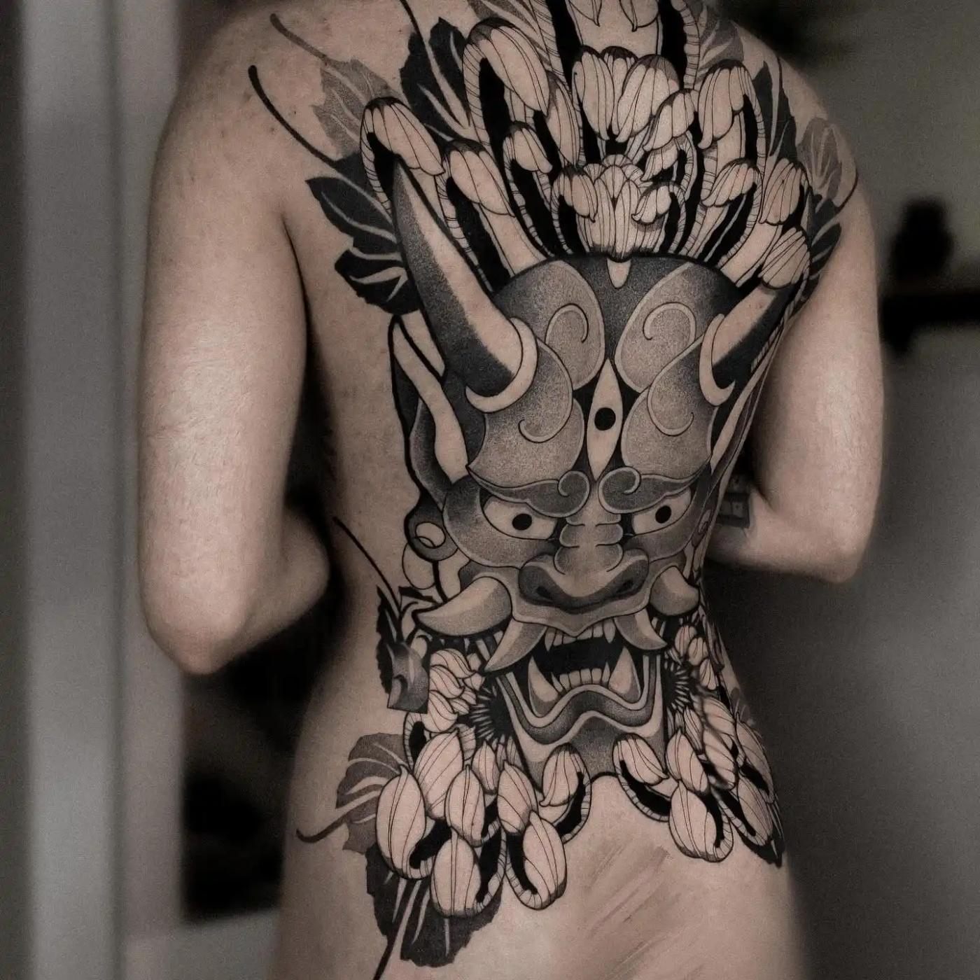 Großes Rückentattoo im japanischen Stil mit einer Oni-Maske, umgeben von kräftigen floralen Elementen, das Blackwork und Dotwork für starken Kontrast und Textur verbindet.