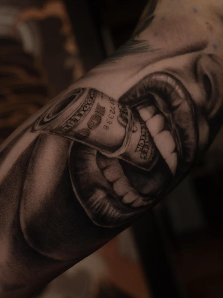 Hyperrealistisches Schwarz-Grau-Tattoo im Chicano-Stil von geöffneten Lippen, die einen gerollten Geldschein umschließen – Symbol für Gier und Versuchung, mit weicher Schattierung am Unterarm.