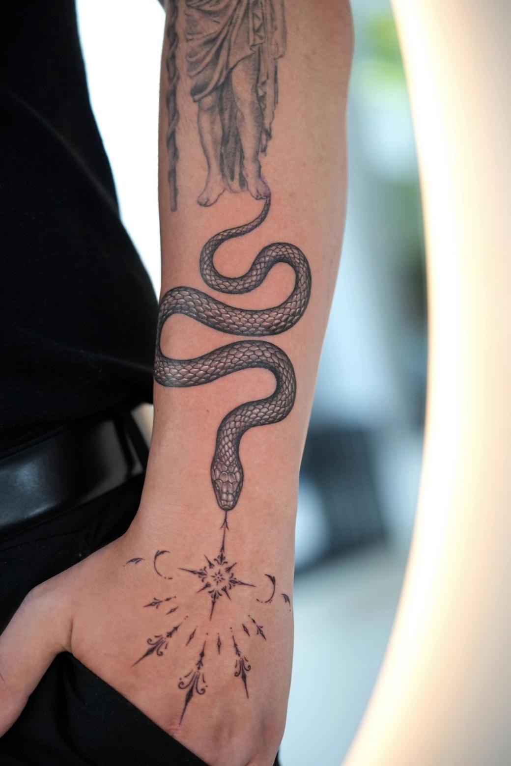 Black and grey tattoo: a snake winding down the forearm to an ornamental star on the back of the hand