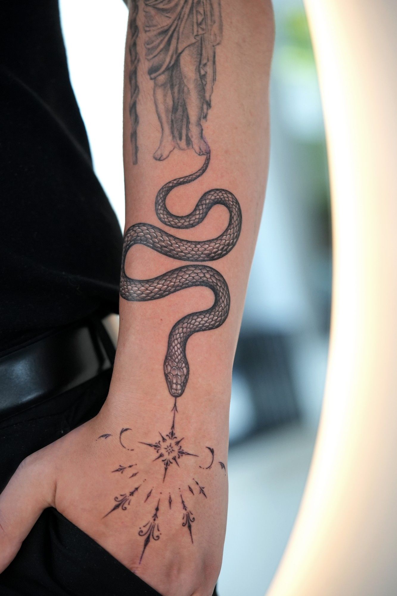 Schwarz-Grau-Tattoo: eine Schlange windet sich den Unterarm hinab zu einem ornamentalen Stern auf dem Handrücken