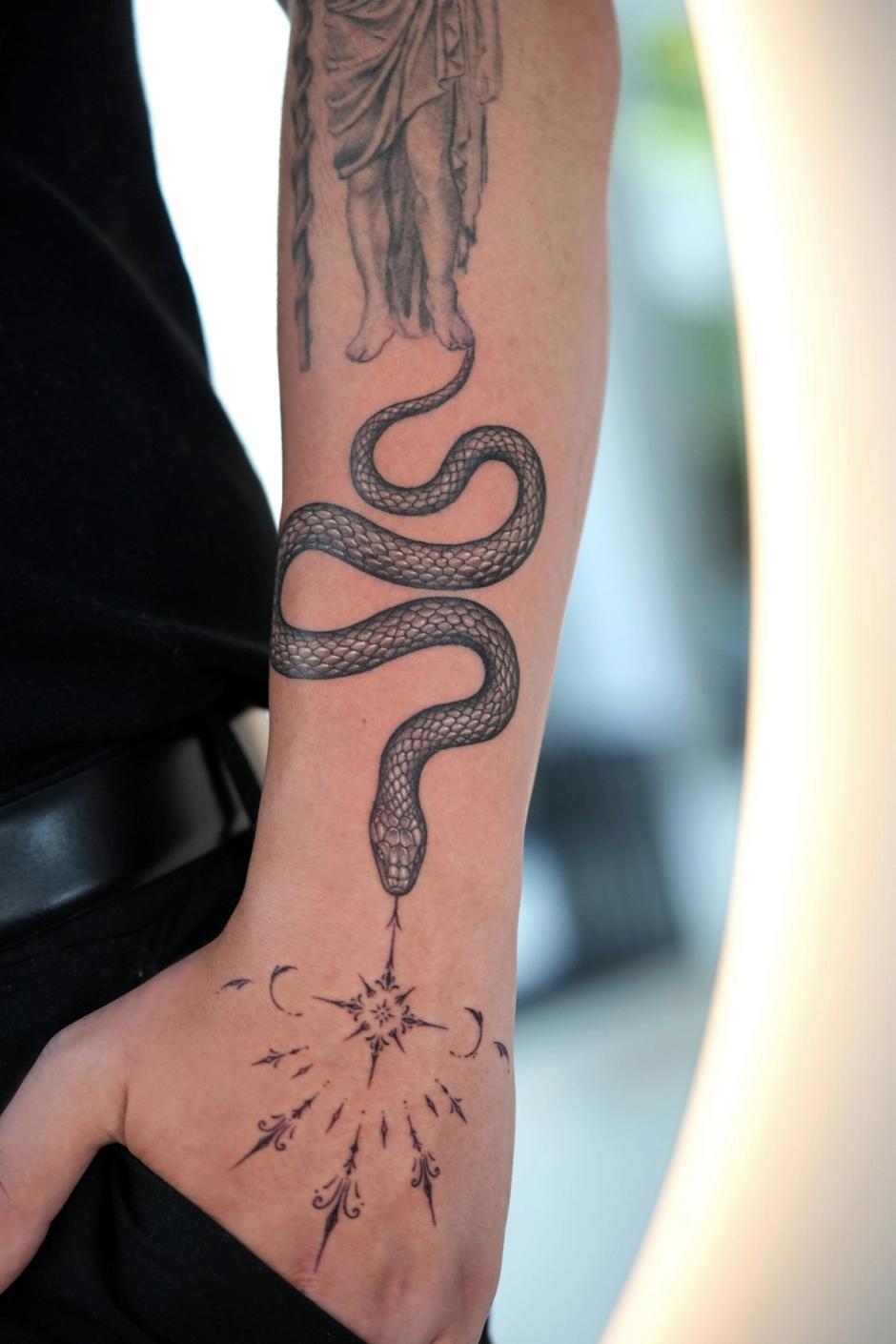 Black and grey tattoo: a snake winding down the forearm to an ornamental star on the back of the hand
